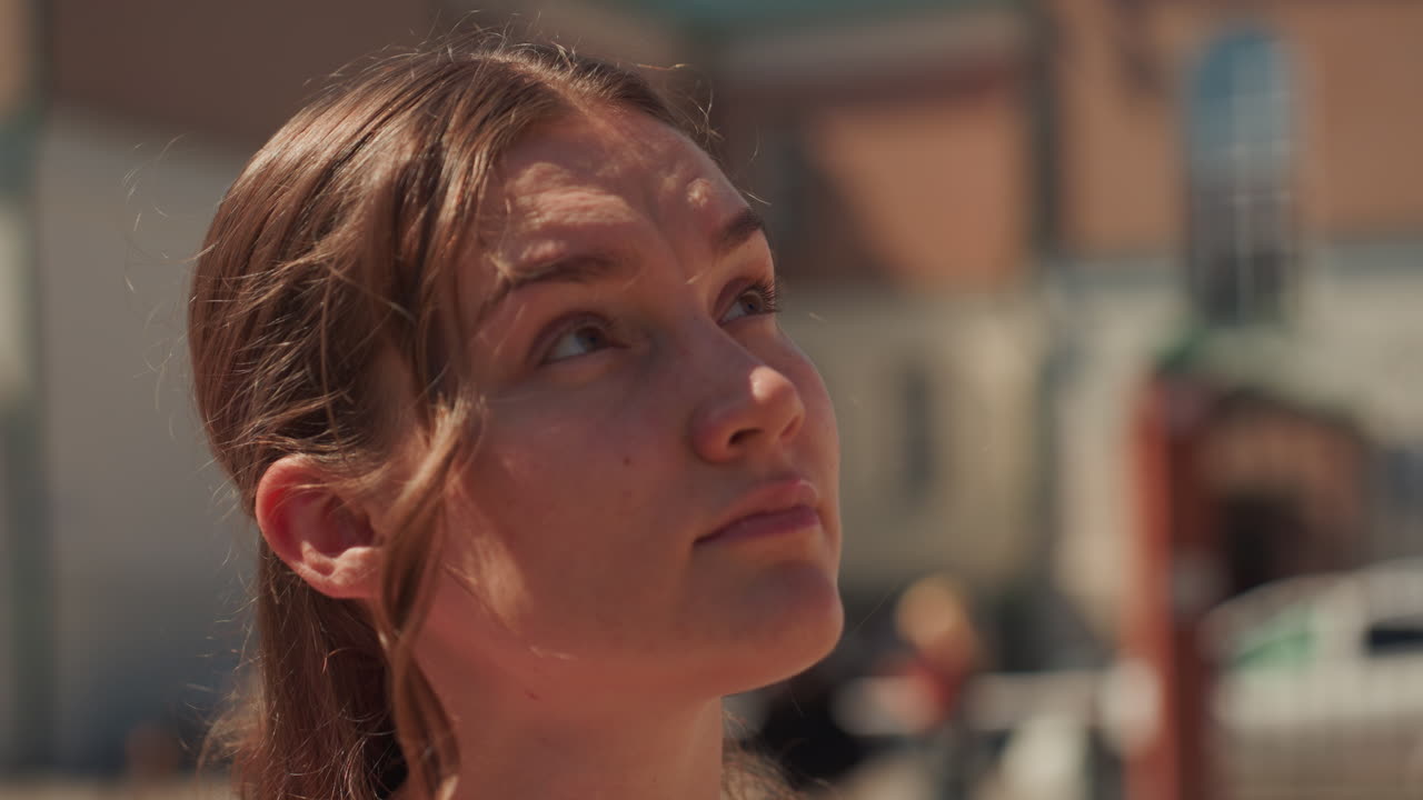 young woman in pink dress smiles under sun, city square backdrop with classical architecture, sunglasses on face, soft golden highlights on skin, candid closeup capturing relaxed gaze and warm summer