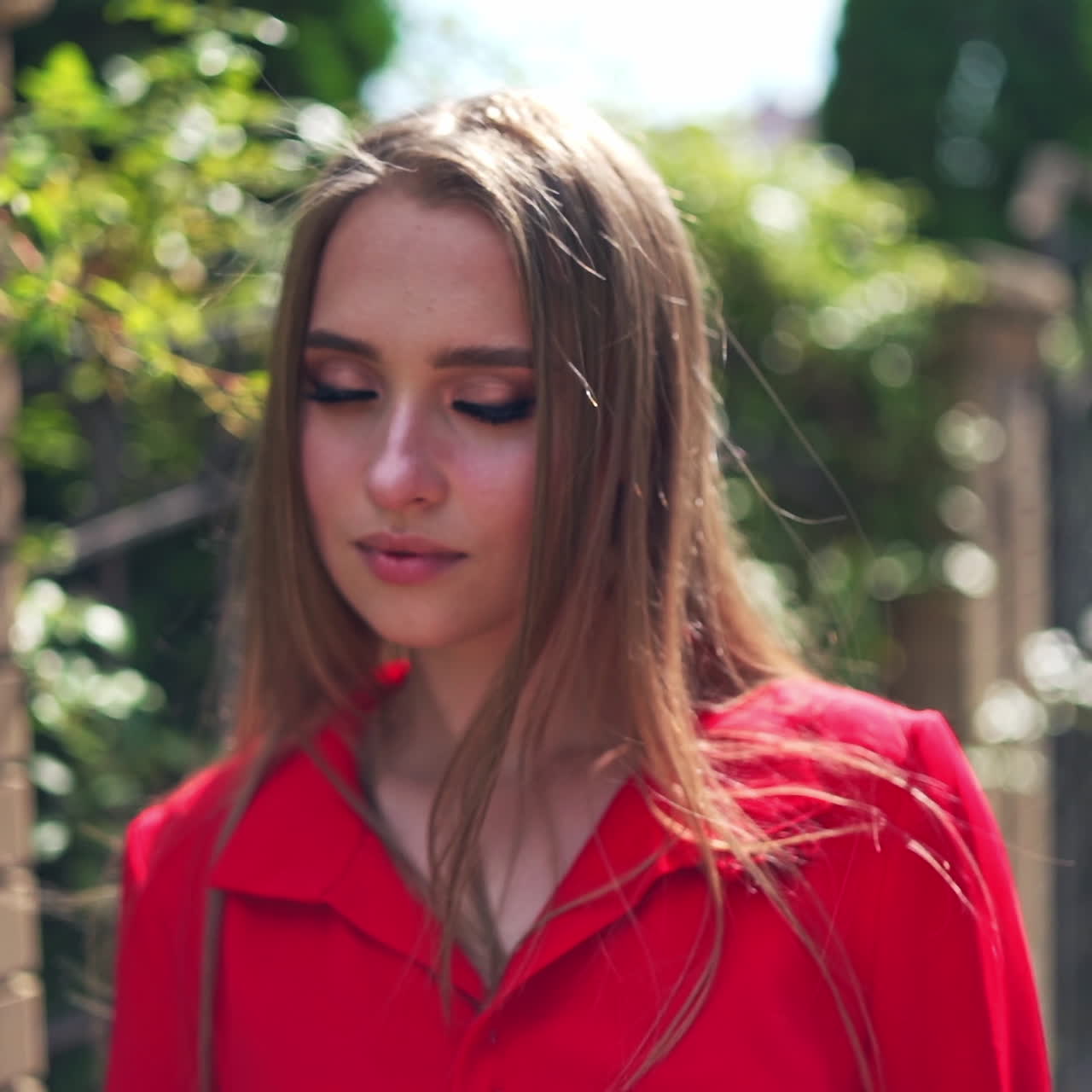 Portrait of beautiful model outdoors. Face of a lovely young woman with long hair in red blouse standing in the street and posing on camera.