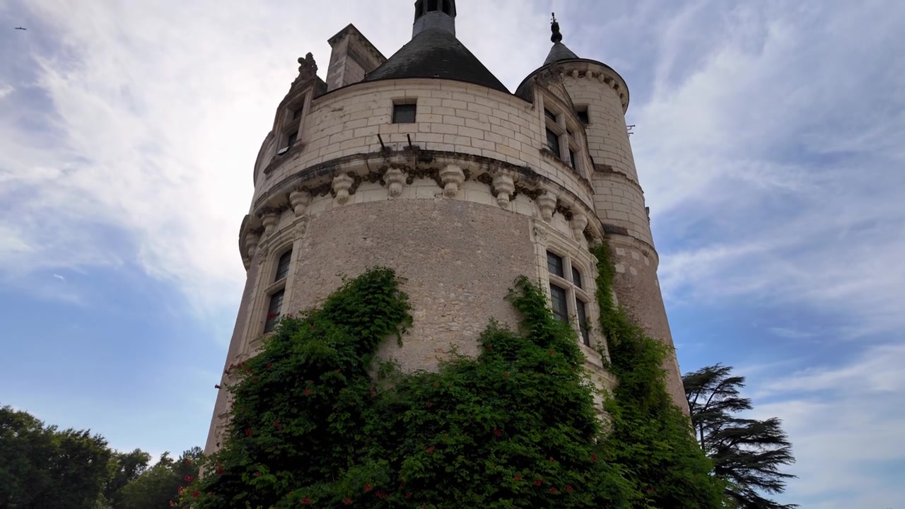 Historyczna kamienna wieża w pobliżu wejścia do Château de Chenonceau, otoczona bujną zielenią i tradycyjnymi budynkami posiadłości