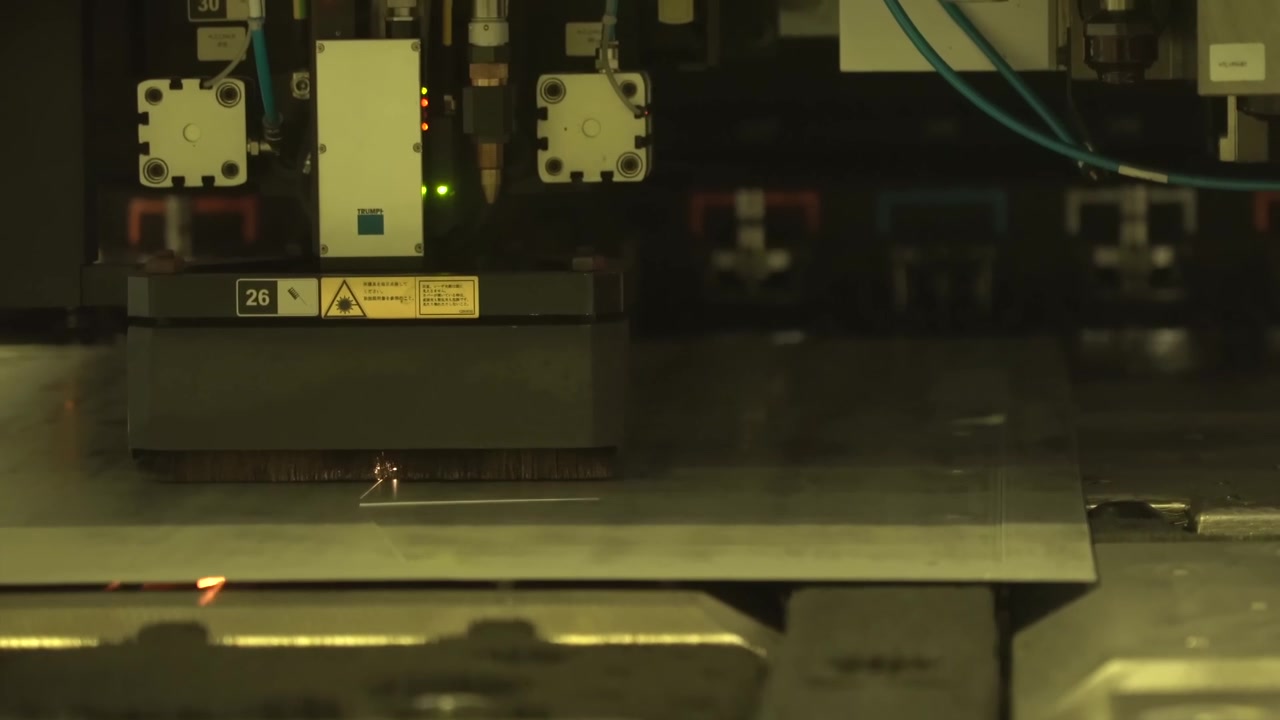 CNC laser cutting machine slicing a thick steel sheet with bright orange sparks flying inside a modern metal fabrication factory