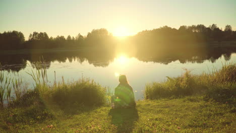 chica solitaria envuelta en cuadros sentada en la orilla del lago y viendo el amanecer