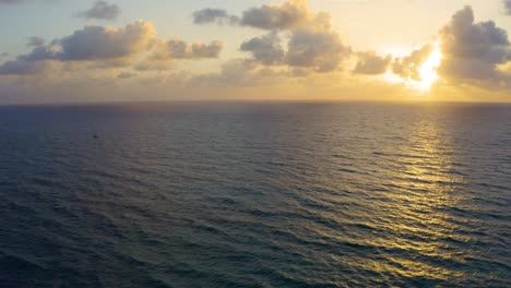 very still aerial drone shot looking towards the sunrise casting rays over the atlantic ocean with a small boat slowly cruising by near palm beach, florida