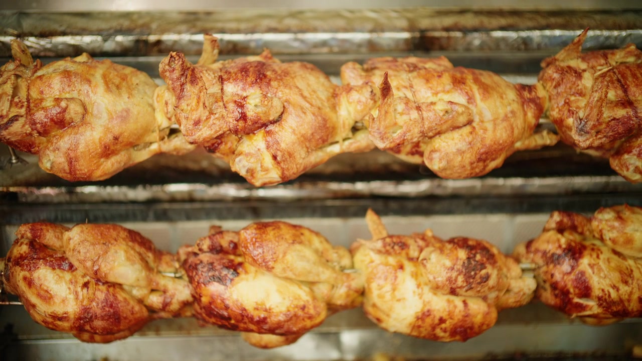 Polli interi che ruotano lentamente sugli spiedi, sviluppando una pelle croccante e dorata in un forno a girarrosto commerciale