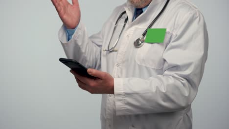 male doctor consults patient using mobile phone. diagnostics of remote examination online using video conference chat. doc in white medical coat with badge with green screen. close up. slow motion