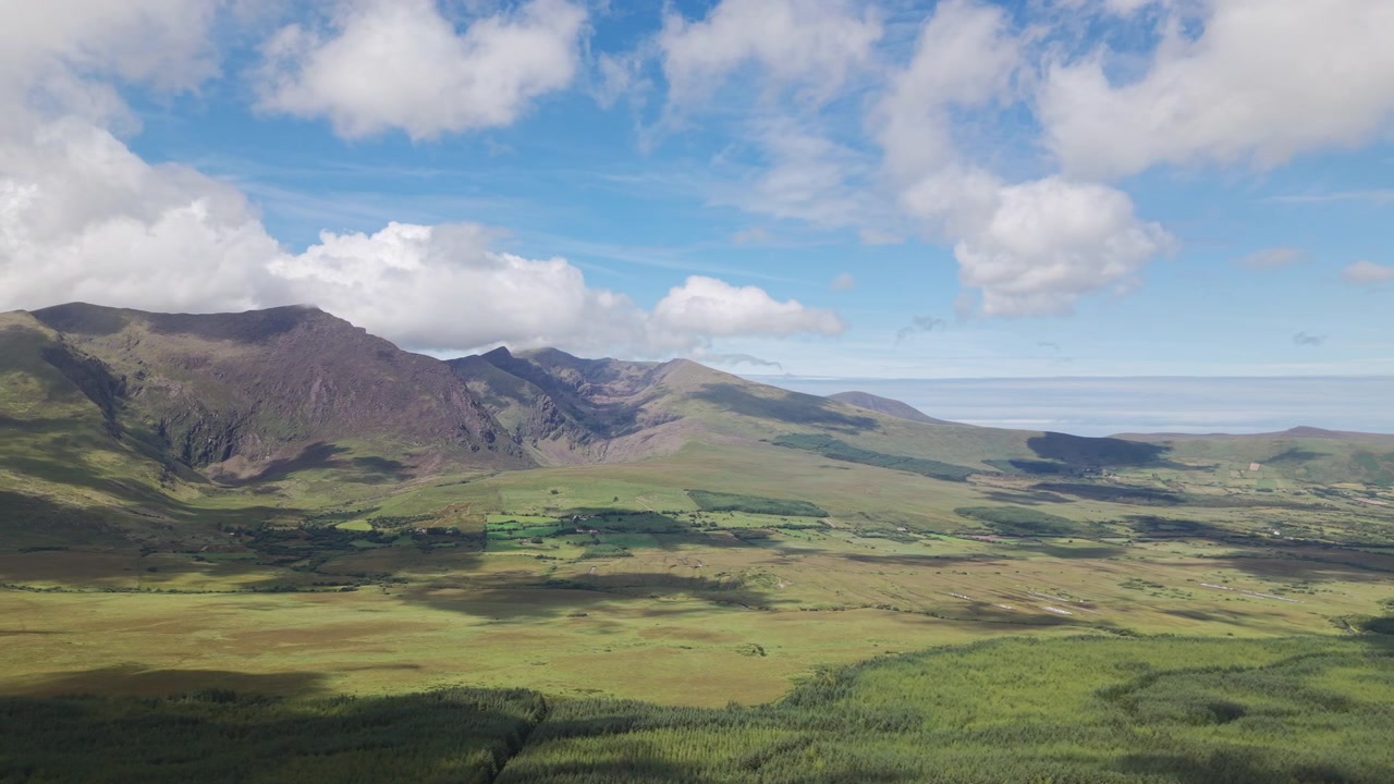 Un'ampia ripresa aerea che mostra le aspre montagne del Conor Pass e le lussureggianti valli verdi sotto un cielo blu. Ideale per documentari di viaggio e narrazione ambientale