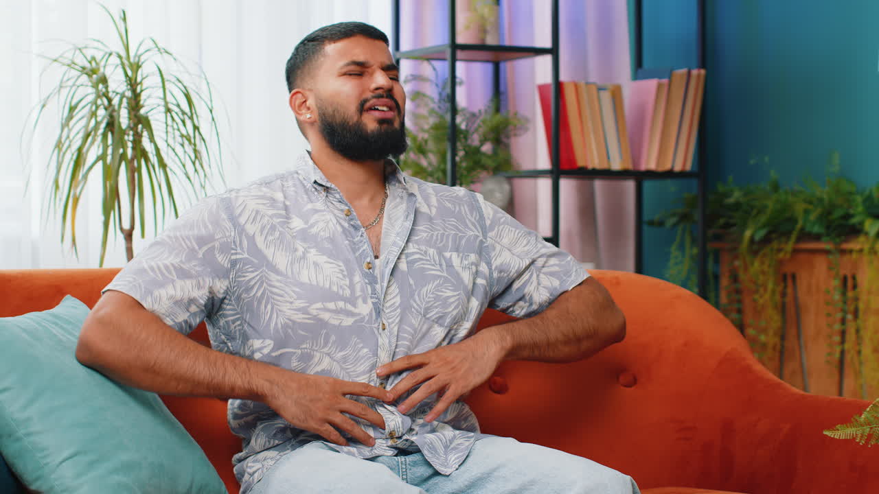 Arabian man sits on sofa feeling sudden strong abdominal stomach ache gastritis problem diarrhea