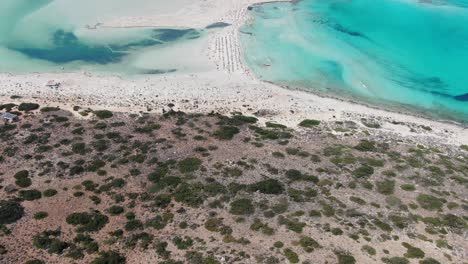 drone view in greece flying over balos beach with clear blue sea water on the sides and white sand surrounded by brown landscape on a sunny day in crete