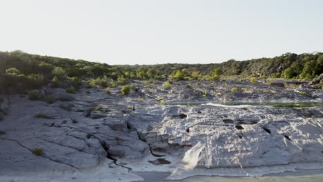 Cinematic-aerial-view-of-drone-going-over-person-walking-across-waterfalls-during-summer-at-sunset