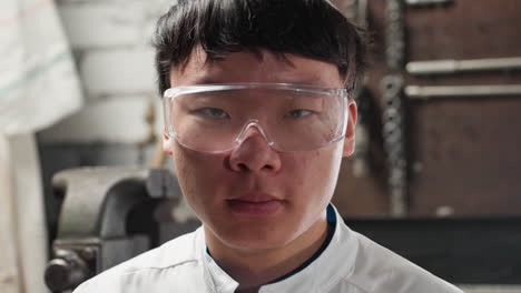 lab technician wearing protective goggles blinks eyes in mechanical workshop, background features industrial tools, bright lighting, and machinery