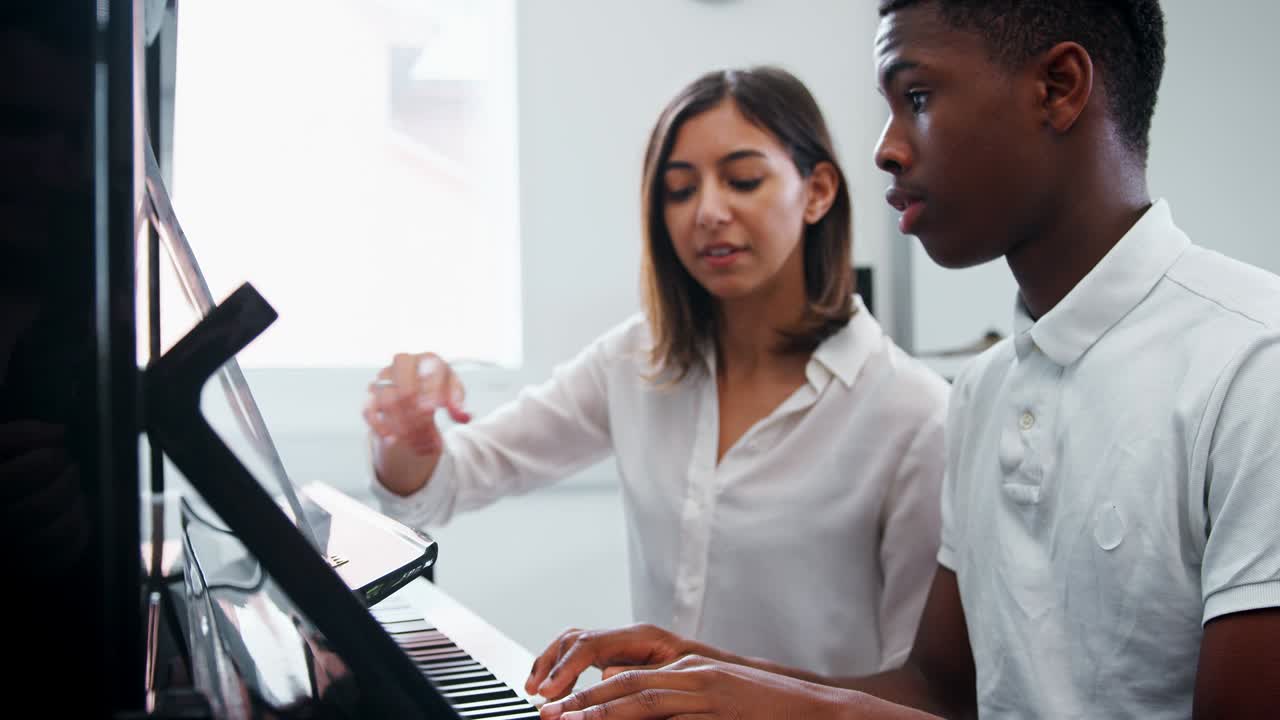 Male Pupil With Teacher Playing Piano In Music Lesson