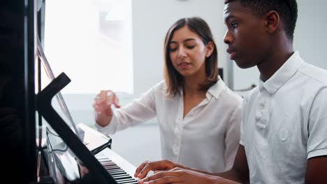 male pupil with teacher playing piano in music lesson