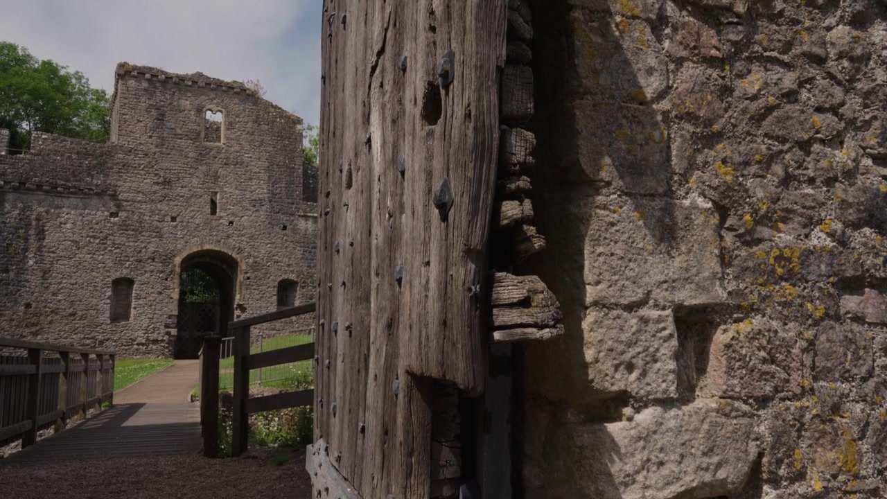Movimento de câmera ascendente revelando portas de madeira históricas no Castelo de Chepstow, começando da base das pesadas pranchas de madeira e inclinando-se lentamente para cima para mostrar a altura total da entrada medieval.