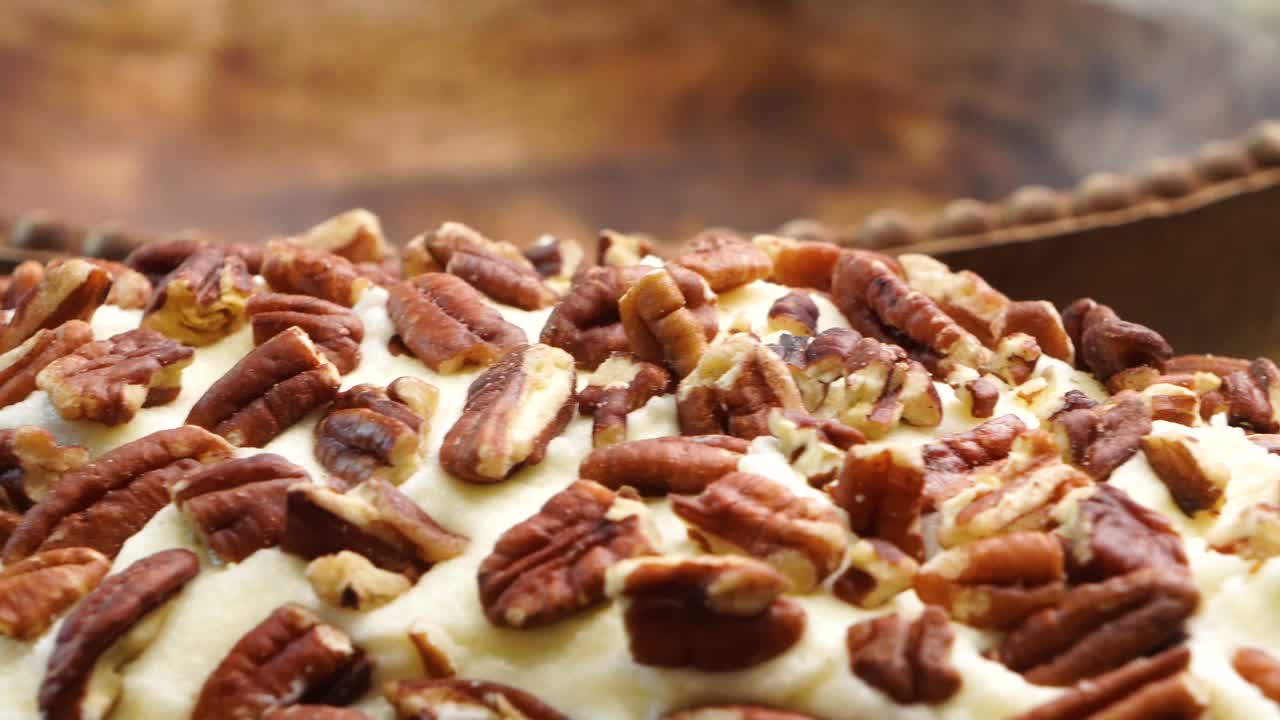 Baking a carrot cake loaf with cream cheese icing and topped with roasted salted pecans. Making a Autumn dessert with carrots, flour, sugar, nuts and frosting. Closeup panning across carrot cake loaf.