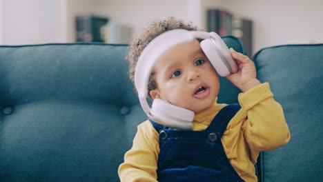 un niño negro lindo con auriculares grandes, sentado en el sofá, tecnología moderna