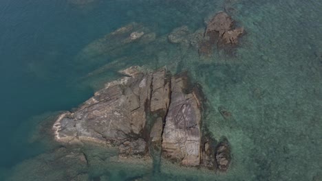 Luftaufnahme-Aus-Der-Vogelperspektive,-Spin-Rotationsschwenk-Von-Granitfelsen-Kommen-Aus-Dem-Klaren-Blauen-Meer-Mit-Korallenriffen-Herum