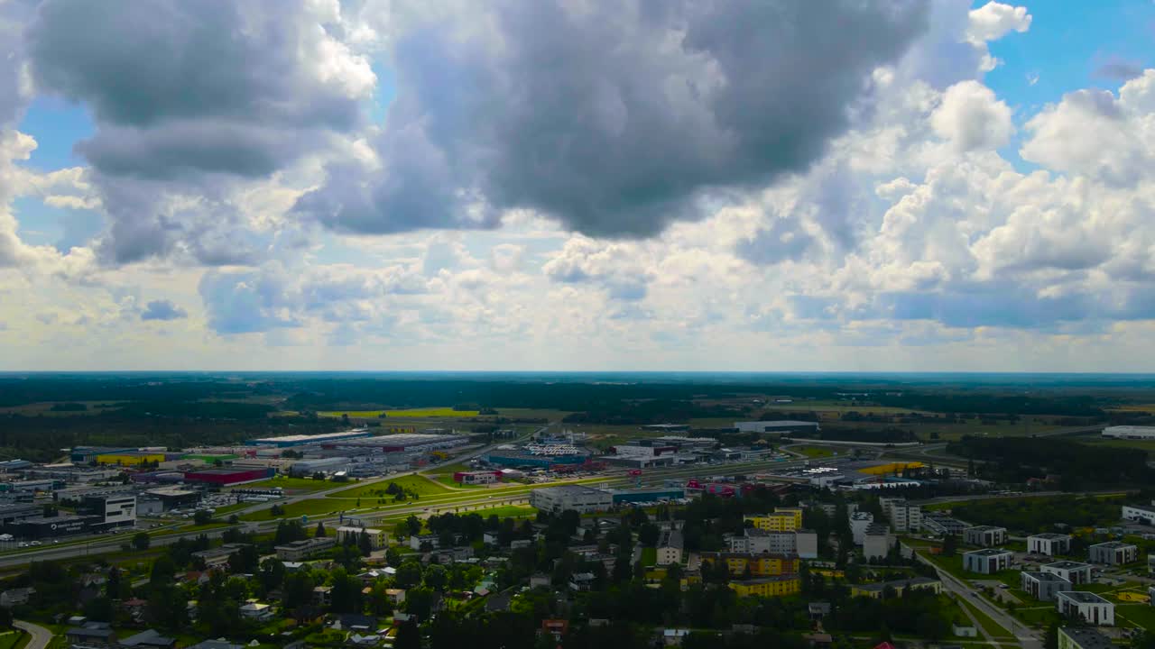 Gorgeous aerial time lapse of white clouds moving fast in a blue summer sky over a small town or a urban city area with a highway going thorugh it where cars and vehicles pass by and drive. Sunpatches