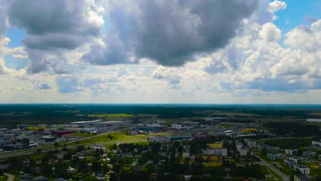 gorgeous aerial time lapse of white clouds moving fast in a blue summer sky over a small town or a urban city area with a highway going thorugh it where cars and vehicles pass by and drive. sunpatches