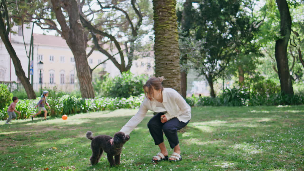 Happy woman playing poodle on green park grass. Girl with furry black puppy