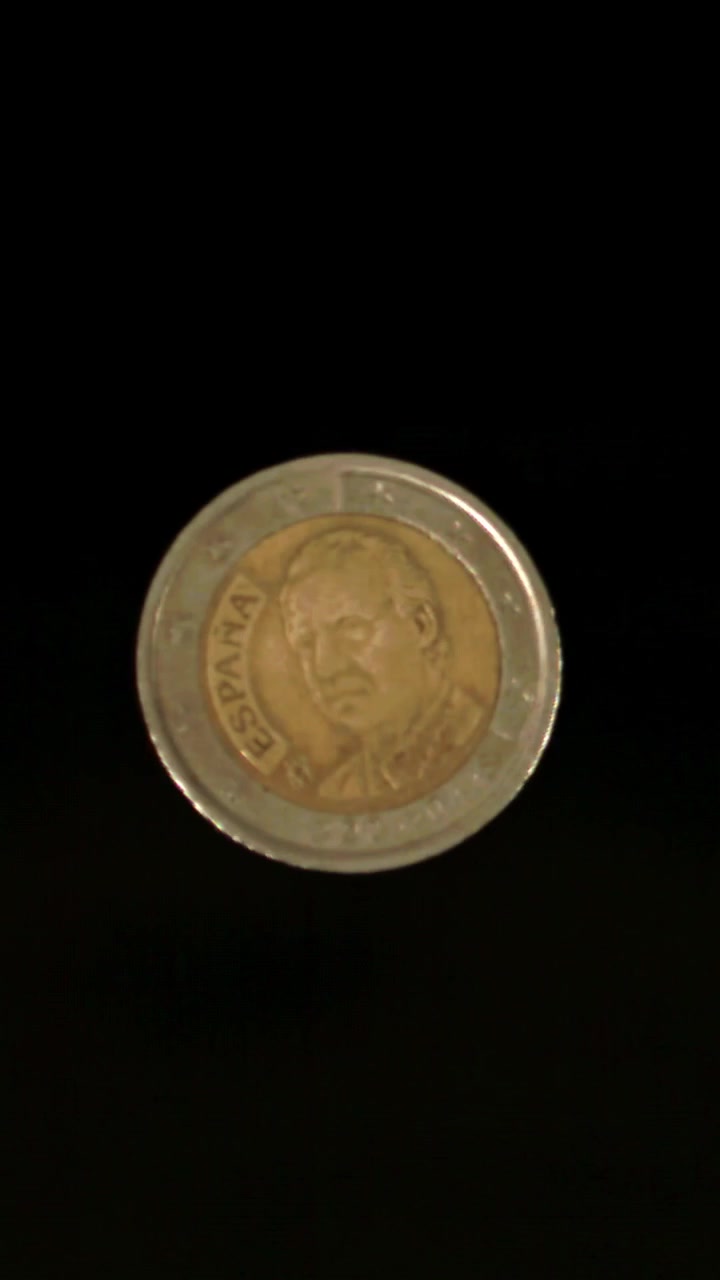 Moneda de 2 euros girando a cámara lenta sobre fondo negro.