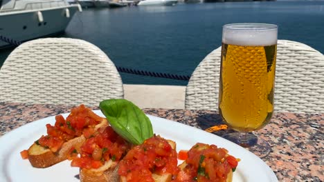 pan clásico italiano bruschetta con tomates y aceite de oliva, vaso de cerveza fría y vista en yates de lujo en puerto banus puerto durante el verano en marbella españa, comida sabrosa, tiro de 4k