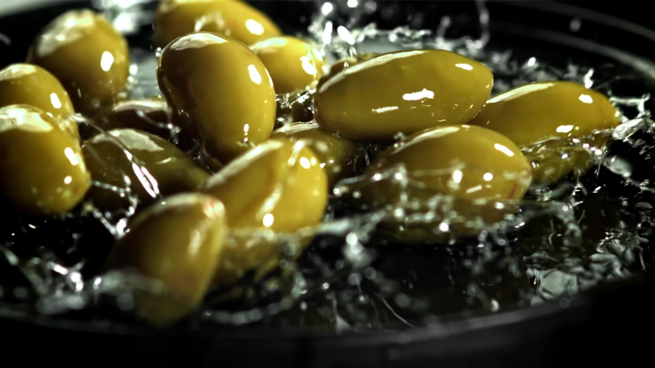 Movimento rallentato di olive verdi che cadono nell'acqua
