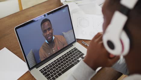 Estudiante-Universitario-Afroamericano-Sosteniendo-Notas-Mientras-Realiza-Una-Videollamada-En-Una-Computadora-Portátil-En-Casa