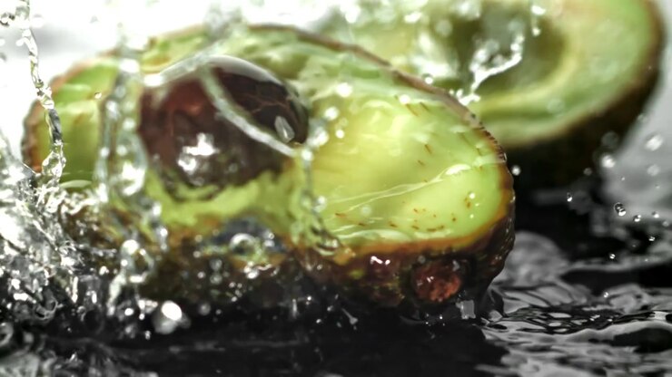Primo piano in slow motion dell'acqua che schizza su un avocado tagliato a metà