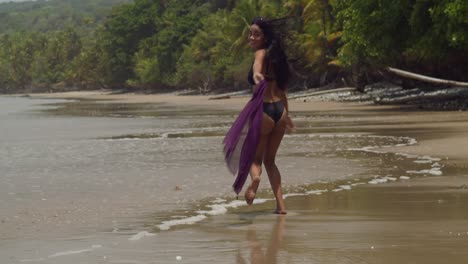 A-sexy-woman-in-a-black-bikini-runs-on-the-beach-and-enjoys-herself-with-ocean-waves-in-the-background