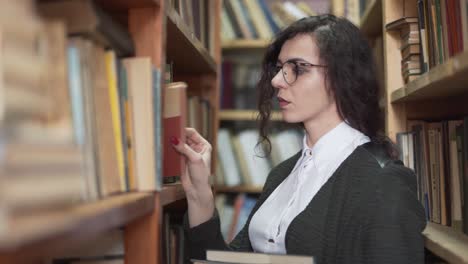 tired serious beautiful teacher picking books from a shelf in a library, medium shot