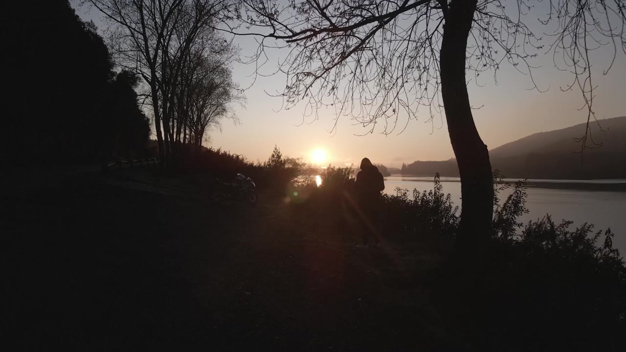 drone shot of sunrise by the lake side of the highway with a silhouette of a visitor and his motorbike