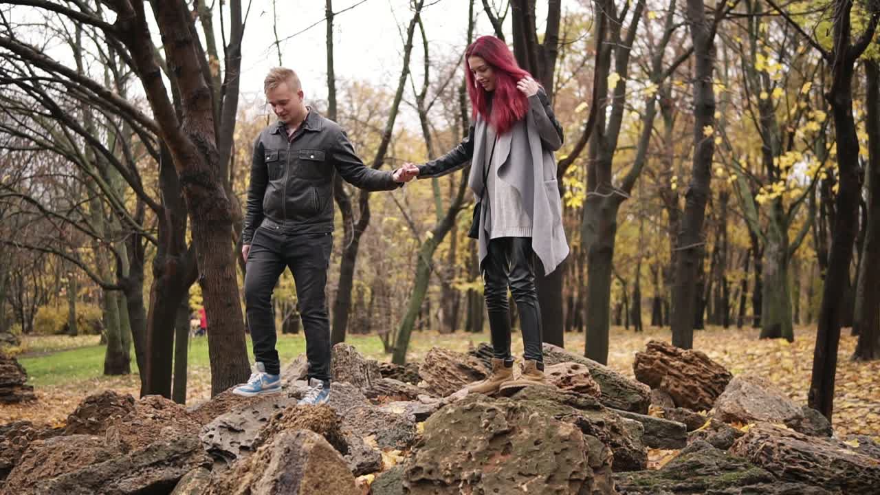 Romantic young couple walking on the rocks in autumn park during the day holding hands. Caring boyfriend is holsing his girlfriend's hand. Warm weather in autumn