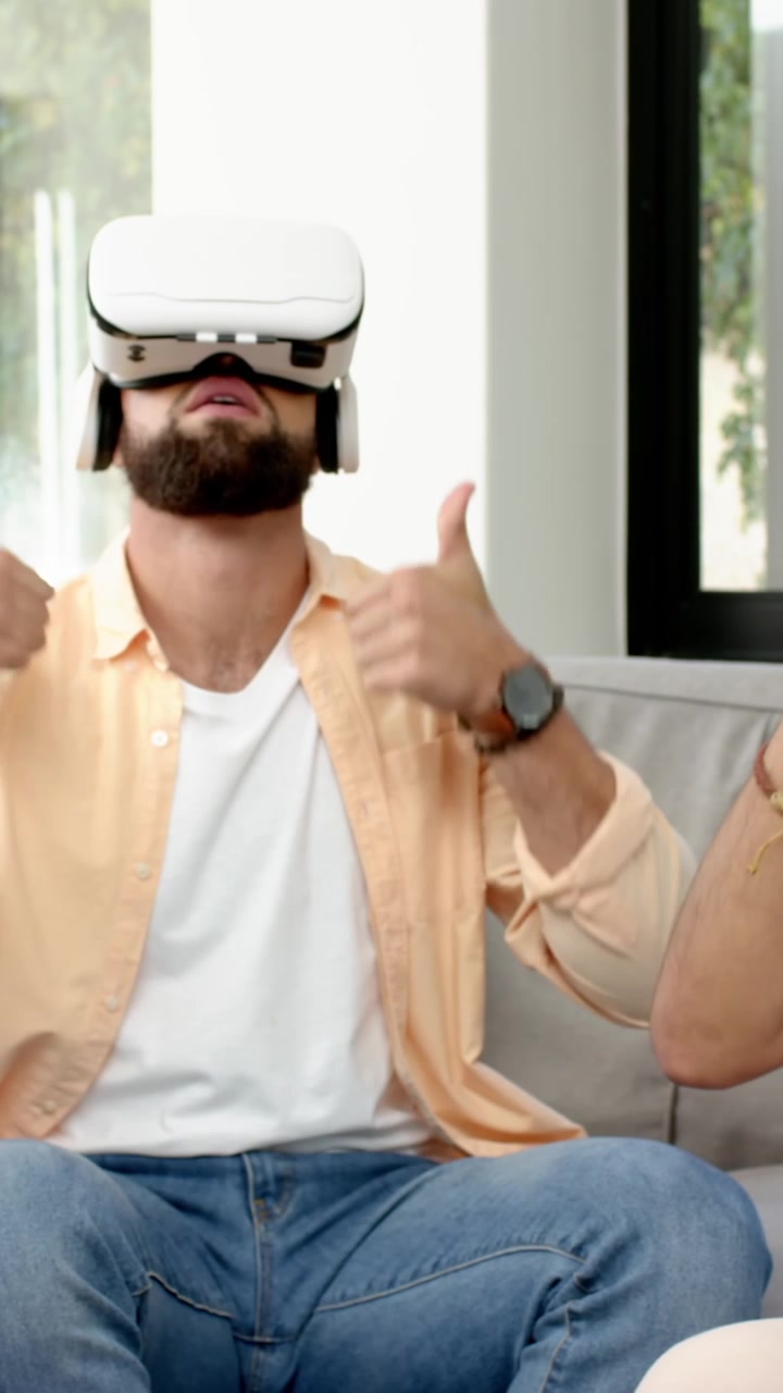 Video verticale: Amici di diverse etnie che allungano la mano per prendere un visore VR bianco sul divano, che testano contenuti VR