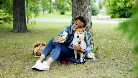 pretty young girl blogger is taking selfie with purebred dog outdoors in city park cuddling and fondling beautiful animal. modern technology, loving animals and nature concept.