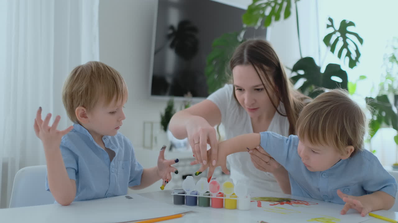 la familia se divierte pintando en el papel con los dedos en la pintura. mamá y dos niños pintan con los dedos en el papel