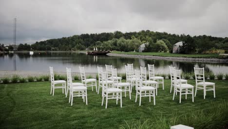 White-wooden-empty-chairs-standing-on-green-lawn-near-lake