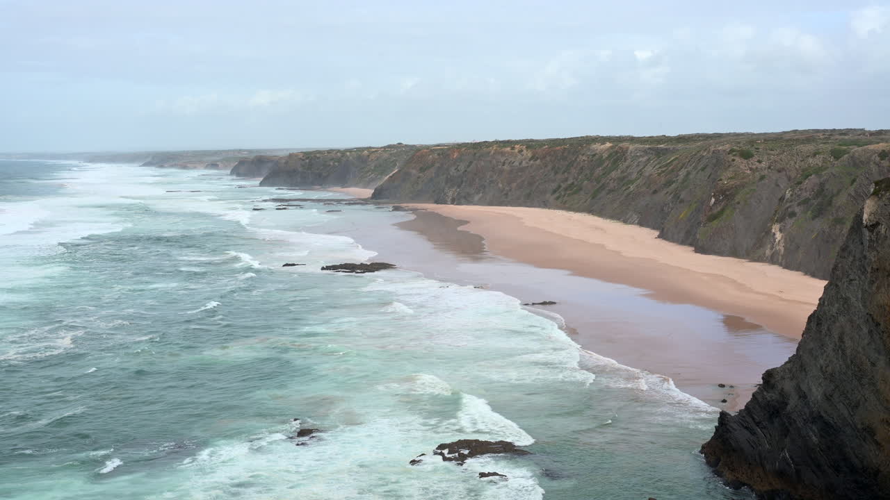 Panning shot from a cliff at North Atlantic coastline with breaking waves