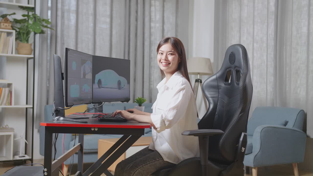 아시아 여성 자동차 디자이너가 스튜디오의 데스크 컴퓨터에서 ev 자동차의 3d 모델을 작업하는 동안 카메라에 미소 짓고 있습니다.