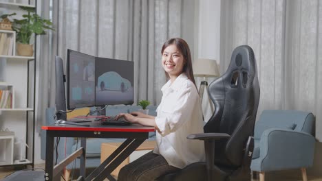 diseñadora automotriz asiática sonriendo a la cámara mientras trabaja en el modelo 3d del coche ev en las computadoras de escritorio en el estudio