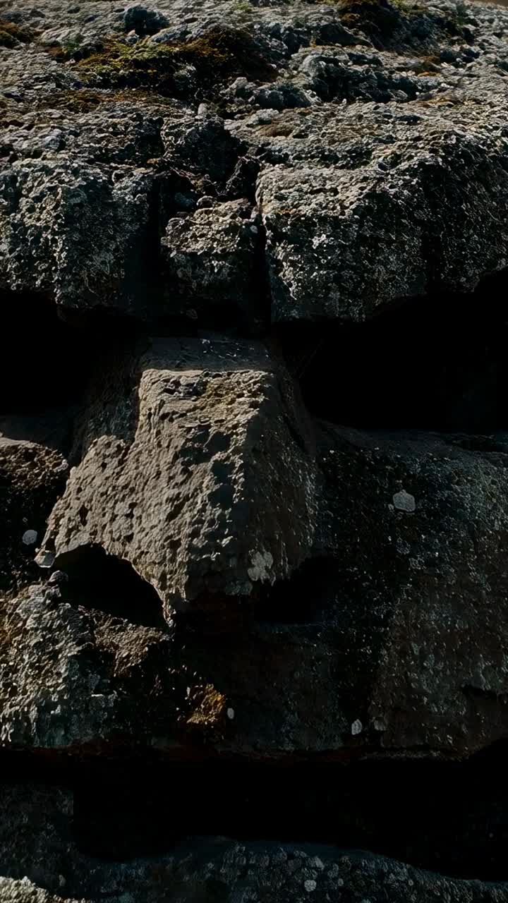 Vertikal video: Bevægeligt kamera, der viser lagdelte sten på bakke, og som afslører central blok, sprækker og mos