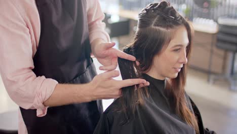 Caucasian-male-hairdresser-holding-female-client's-hair-and-advising-her-at-salon,-slow-motion
