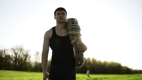 A-handsome-man,-an-athlete-carries-coiled-battle-ropes-on-his-shoulder-after-training-in-the-park.-Crossfit.-Sunny-background