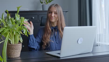 In-office,-brunette-with-long-hair-working-at-laptop-and-waving-at-camera