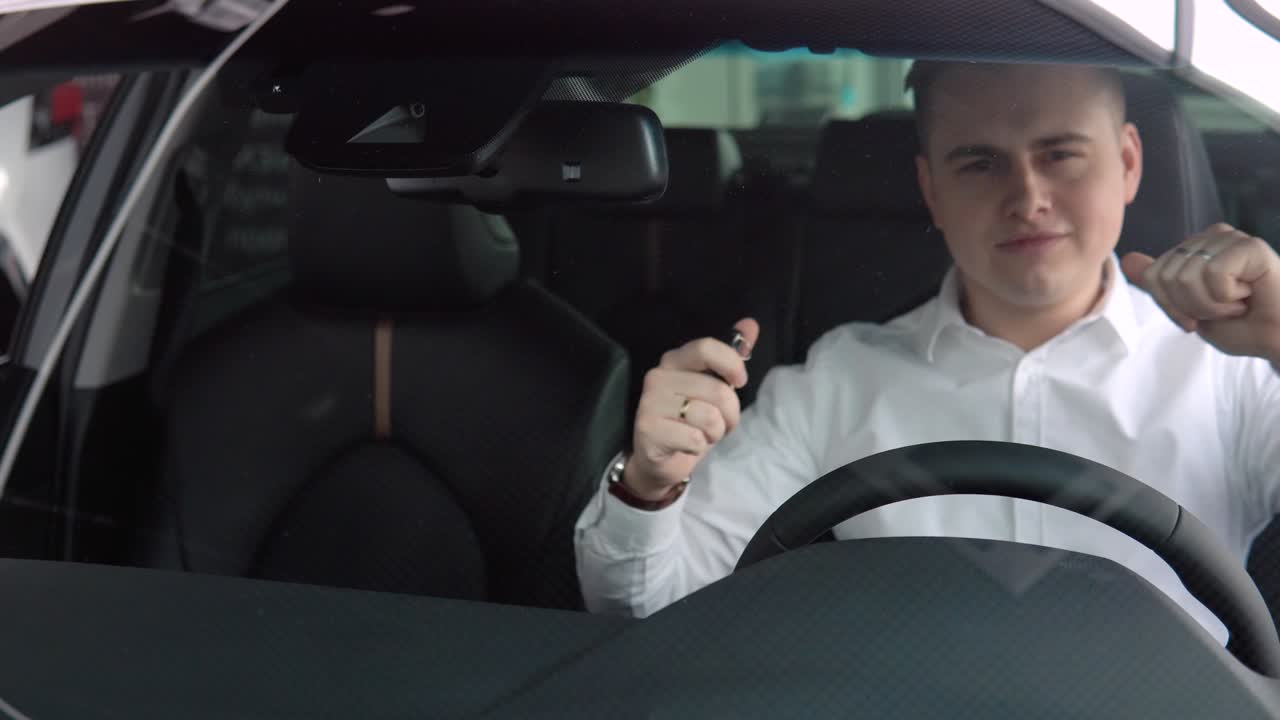Cheerful man rejoices in buying a new car. A man smiles and dances in a new car at a car dealership