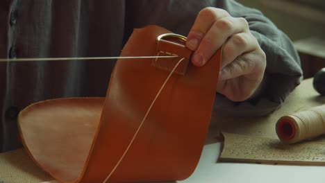 close-up of the process of sewing the handle attachment of a leather bag. the hands of the tailor put the thread in the holes