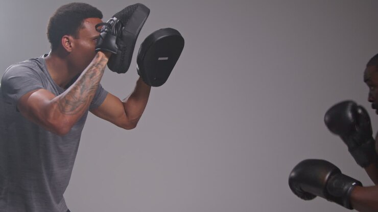 Studio Shot Of Male Boxer Sparring Working Out With Trainer Wearing Punch Mitts Or Gloves Practising For Fight 1