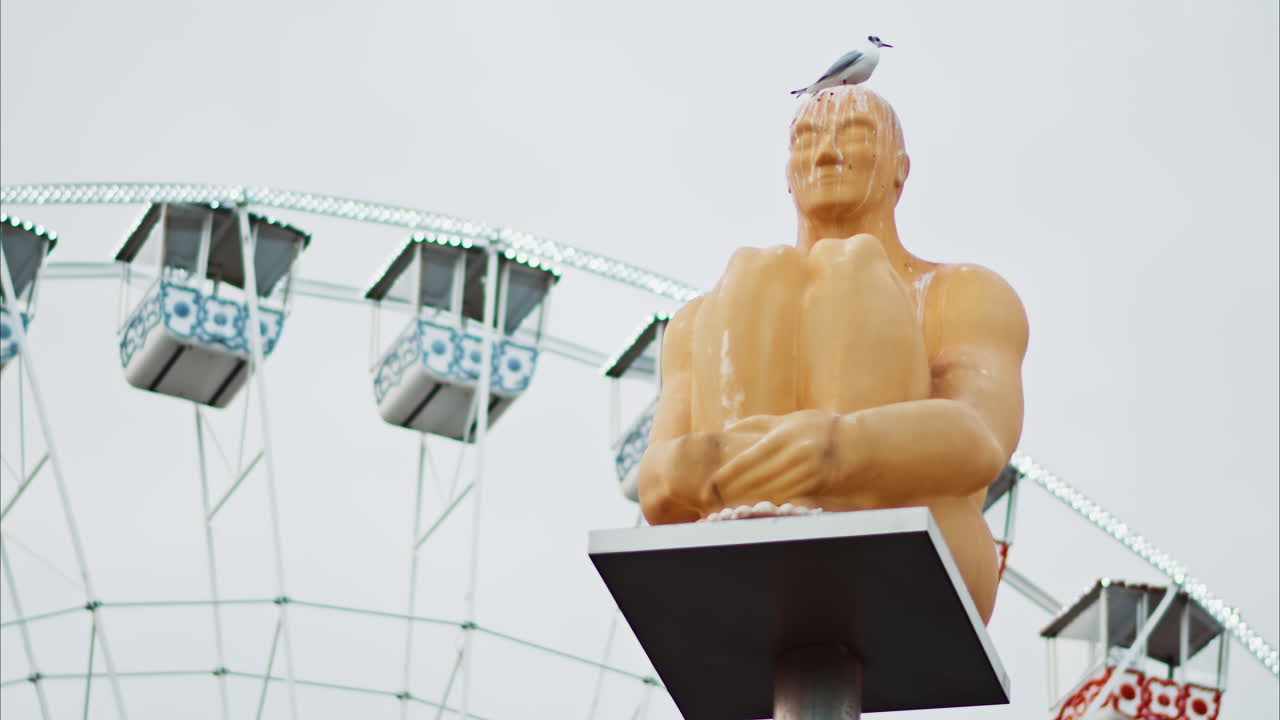 Nice, France - December 8, 2024: Seagull standing on the Conversation a Nice statue by Jaume Plensa at Place Massena with a ferris wheel on the background