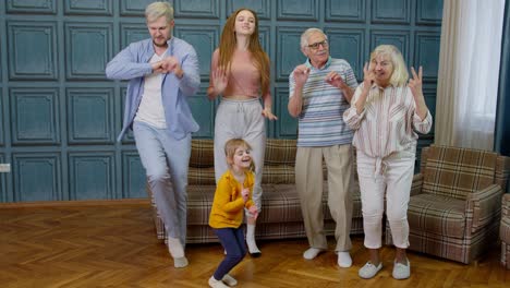 family members of different generations having fun listening music, dancing crazy in room at home