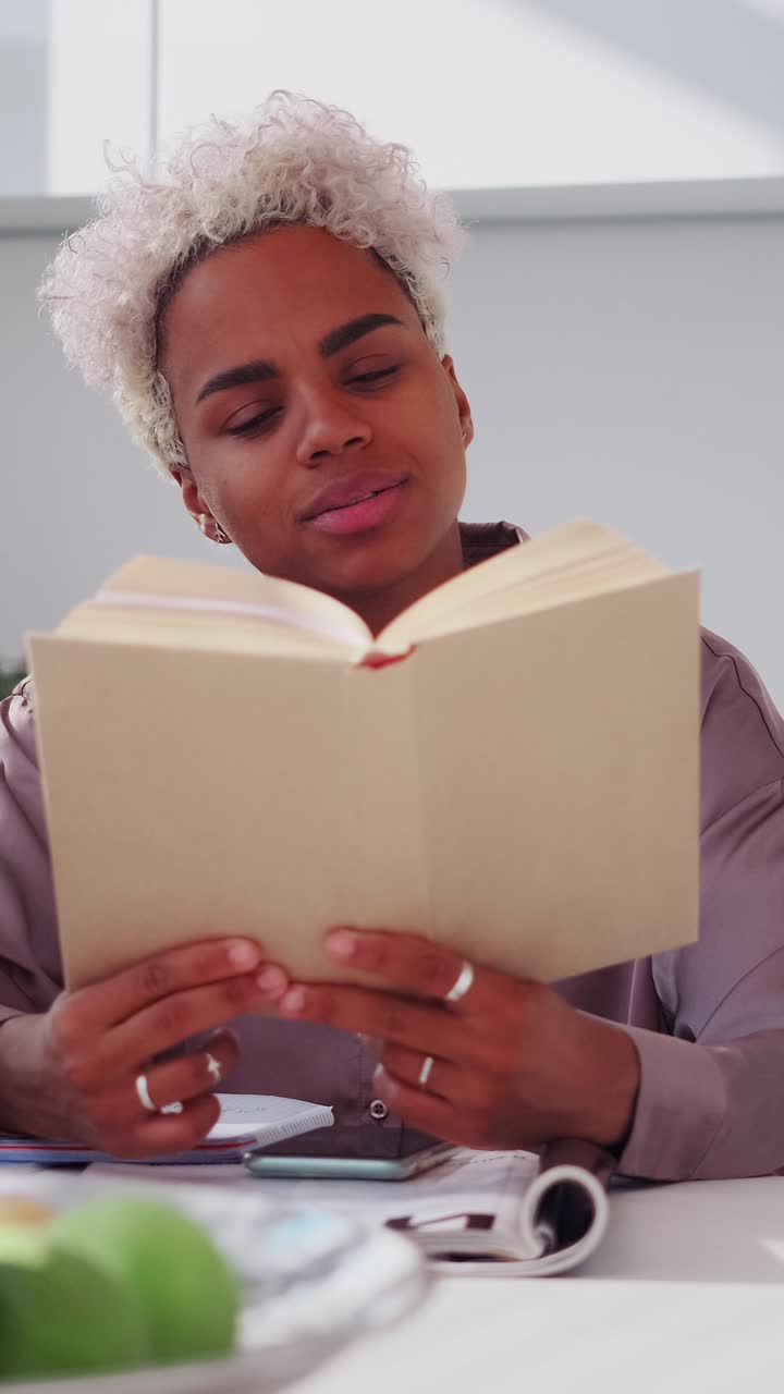 Young professional woman reads a book and smiles while seated at a cluttered
