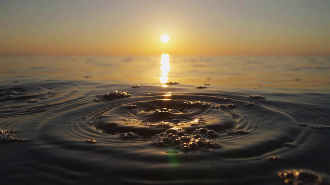 Rising bubbles making rings, front water moving outward at shore, with sun reflection, foam, flare