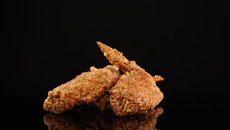 golden-brown fried chicken wings rotate smoothly on a reflective black surface, illuminated by studio lighting for a dramatic, appetizing presentation with seamless camera movement